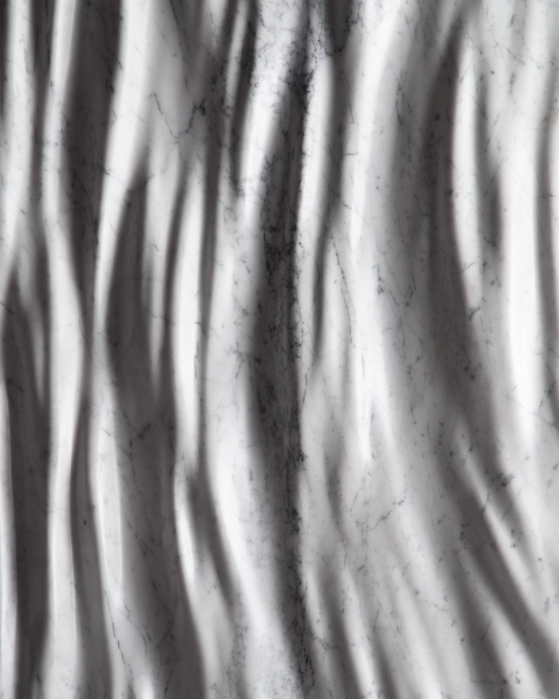 Close up of the Eternal Carrara marble sculpture showing vertical carved folds and soft shadows
