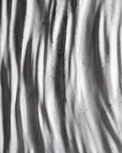 Close up of the Eternal Carrara marble sculpture showing vertical carved folds and soft shadows