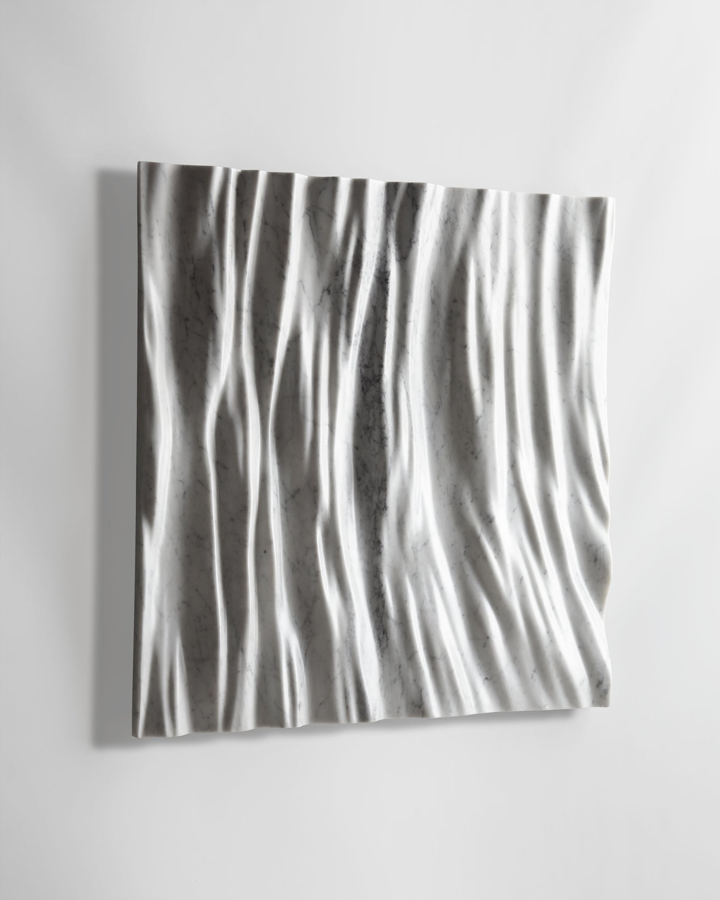 Angled view of the Eternal Carrara marble wall sculpture showing carved depth, soft shadows, and sculpted edge detail
