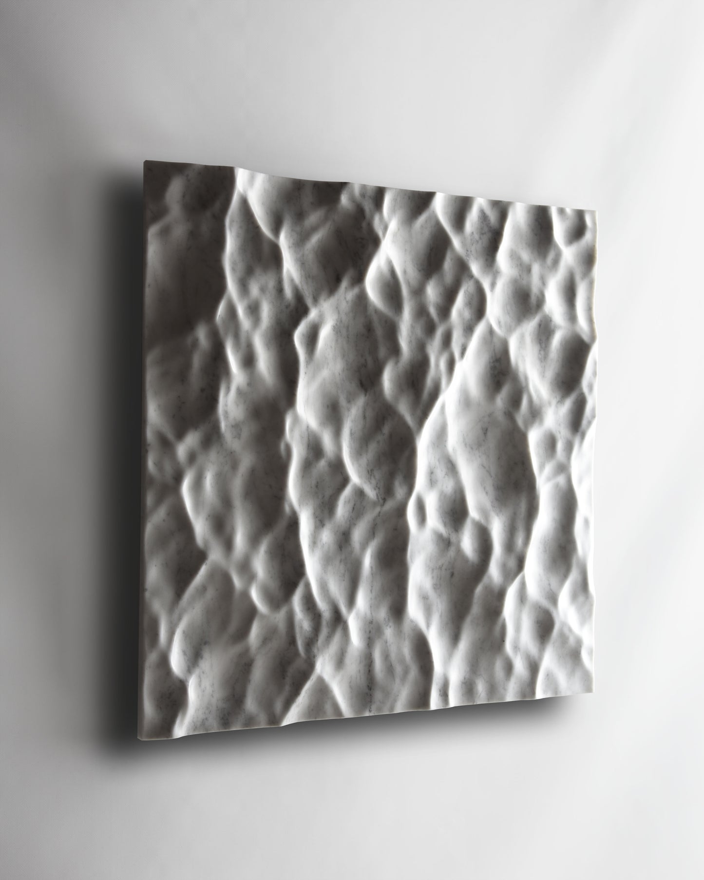 Angled view of the Liquid Marble Carrara wall sculpture installed on a white wall