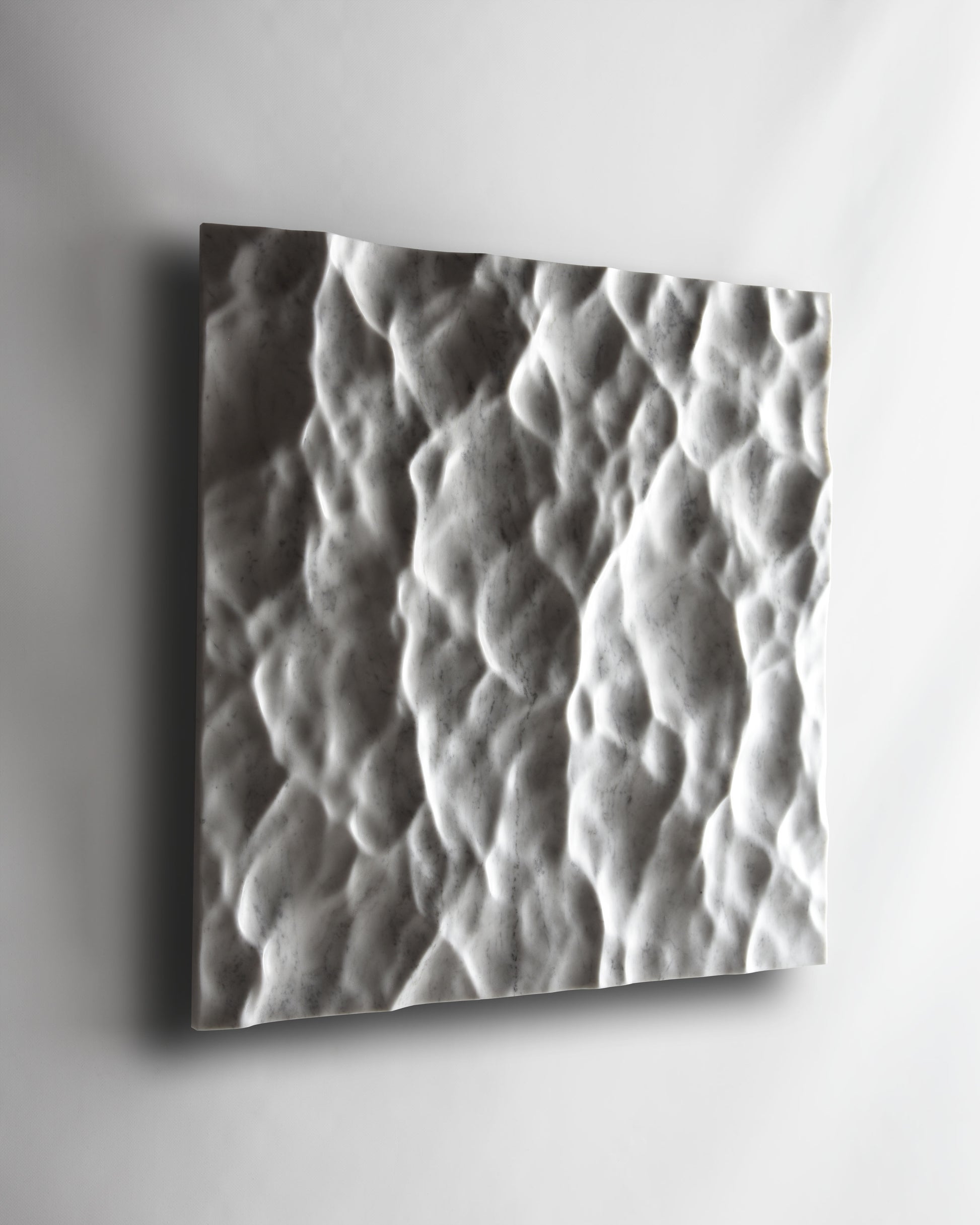 Angled view of the Liquid Marble Carrara wall sculpture installed on a white wall
