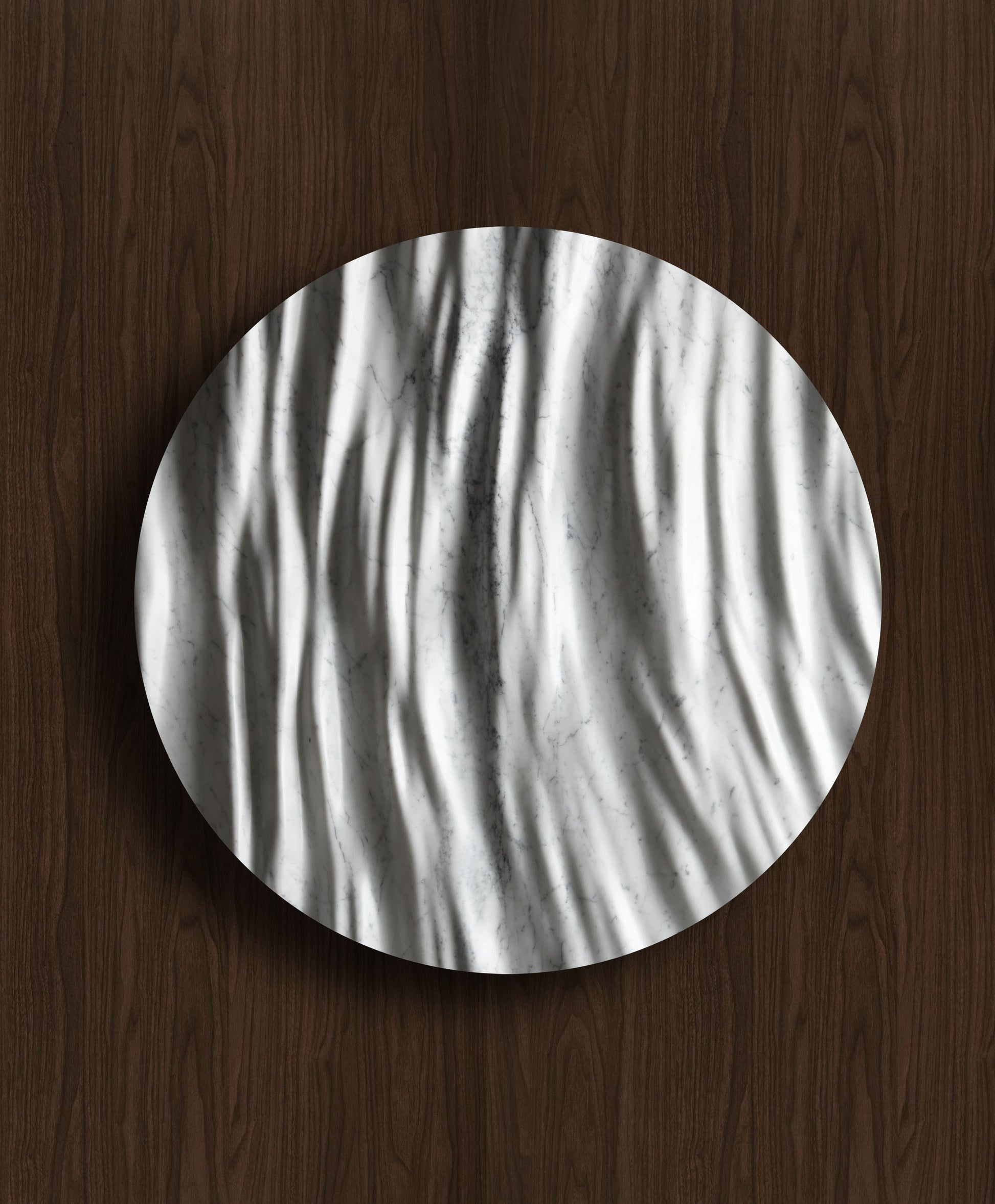 Round Eternal Carrara marble wall sculpture displayed on a warm walnut background with sculpted folds and natural veining