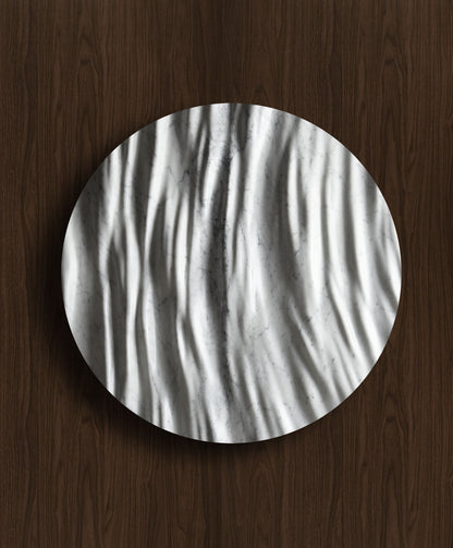 Round Eternal Carrara marble wall sculpture displayed on a warm walnut background with sculpted folds and natural veining