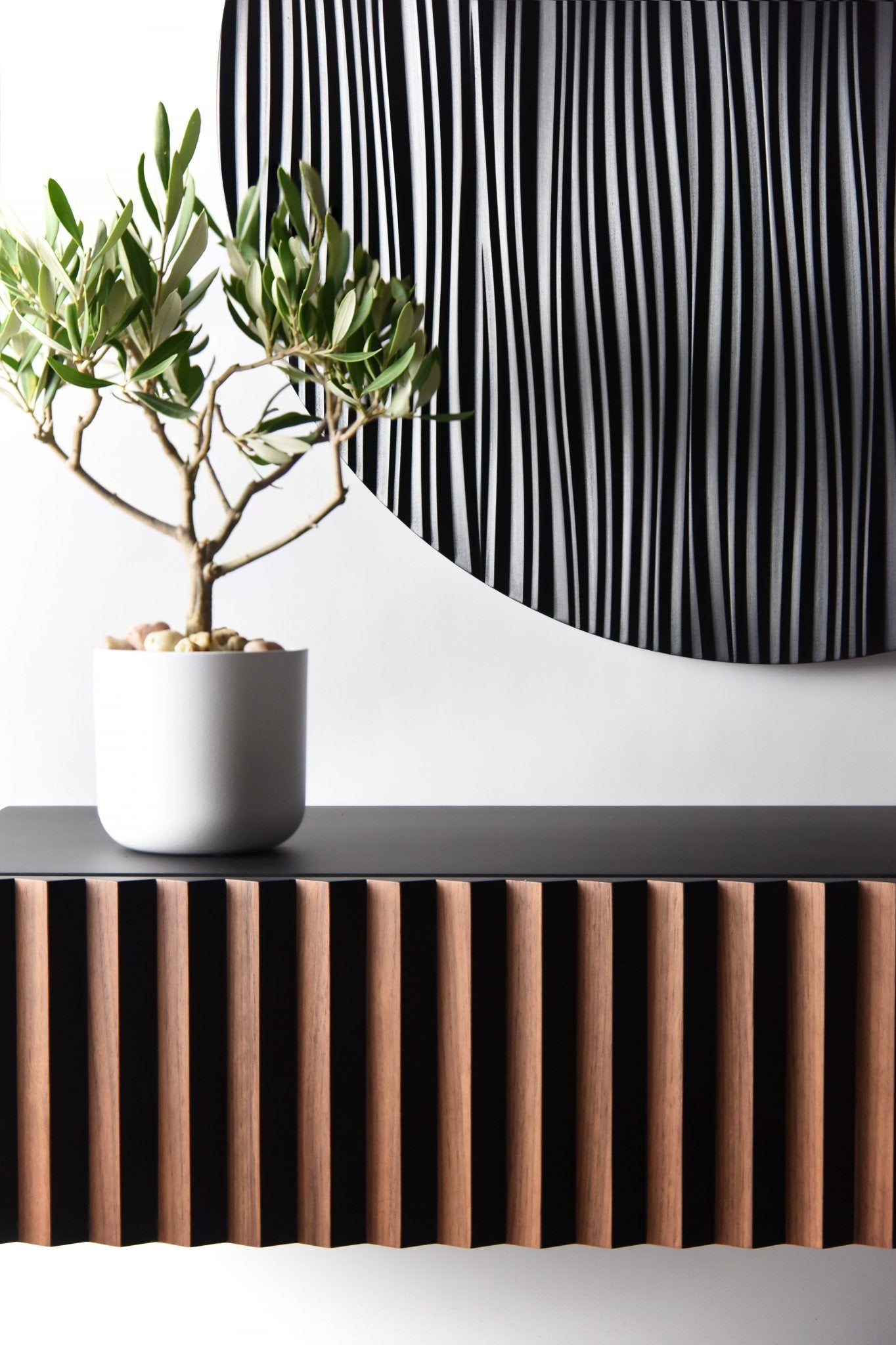 Styled detail showing the walnut and black console front with a plant and soft light