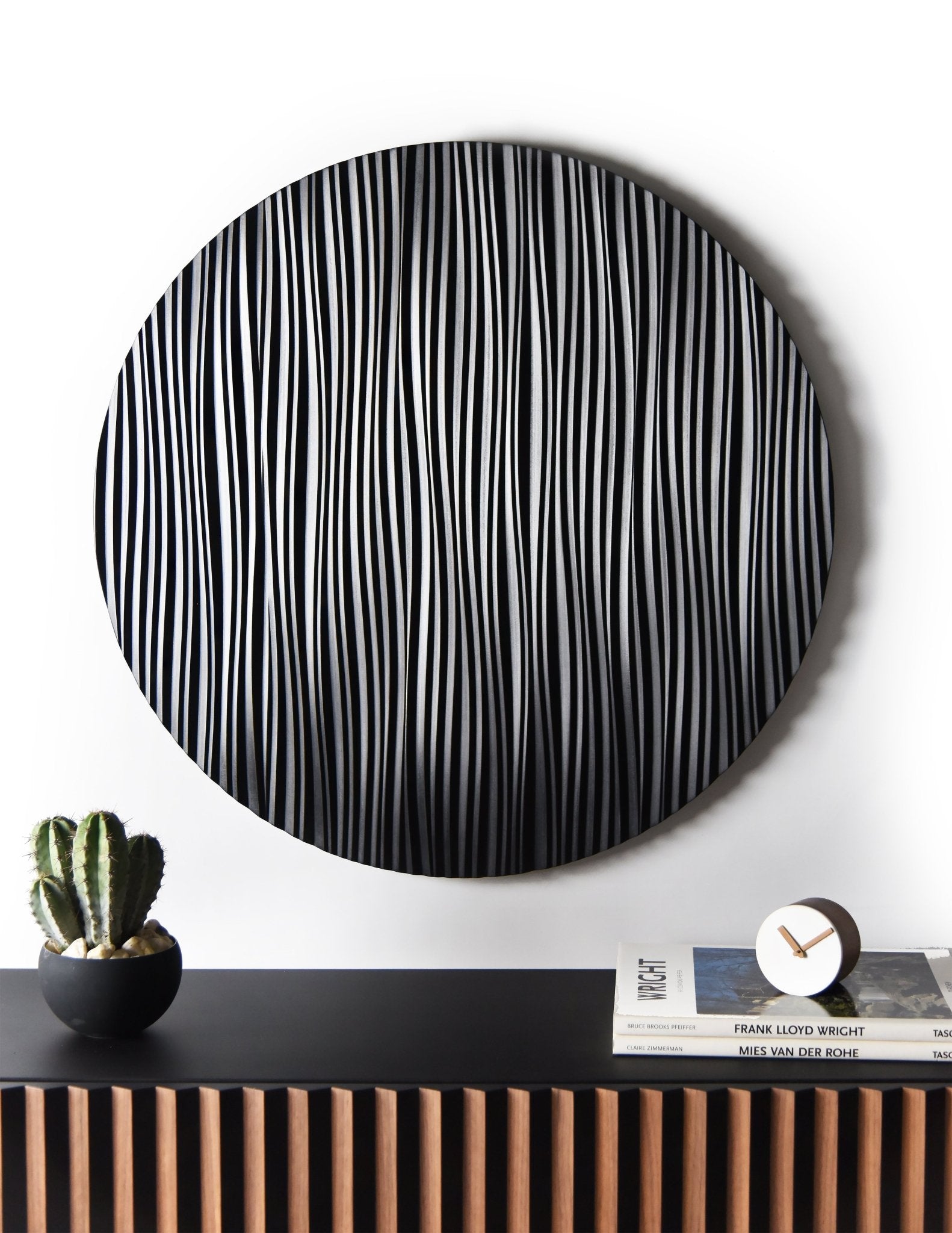 Floating walnut and black console with round Wave wall sculpture installed above in a minimal interior